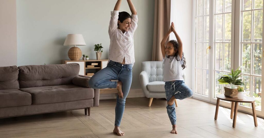Indian mother and daughter practicing yoga together in their living room.