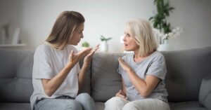 Young woman (daughter) and older woman (mother) sitting on a couch arguing with each other.