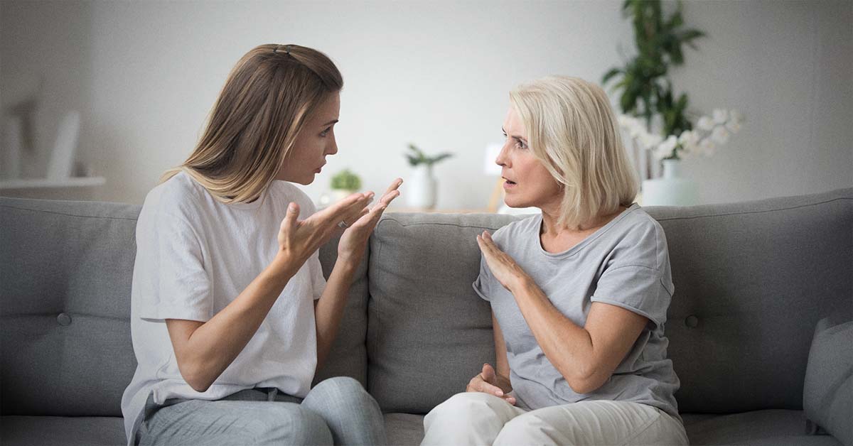 Young woman (daughter) and older woman (mother) sitting on a couch arguing with each other.